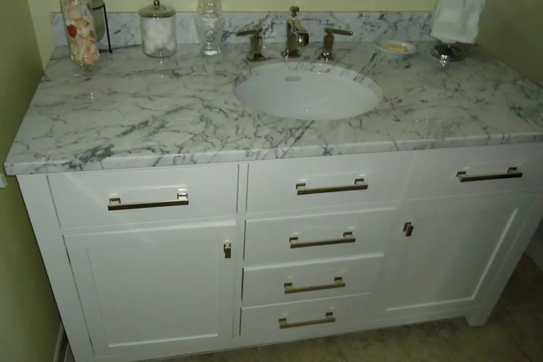 A white shaker bathroom vanity with a marble countertop and brass bar pulls in a Southern California home near San Clemente CA