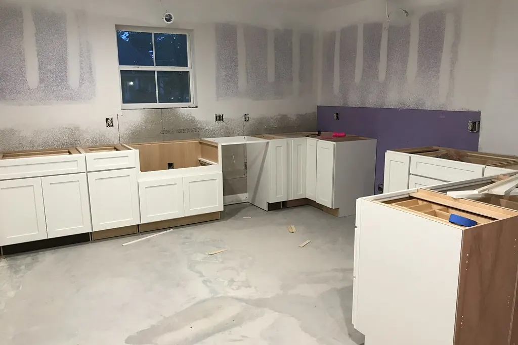 White cabinet boxes set against primed drywall on a bare slab during a kitchen installation in a San Clemente CA style home