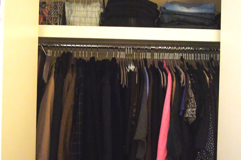 A reach-in closet with a hanging rail, an upper shelf and wire storage baskets in a bedroom of the kind found in San Clemente CA tract housing