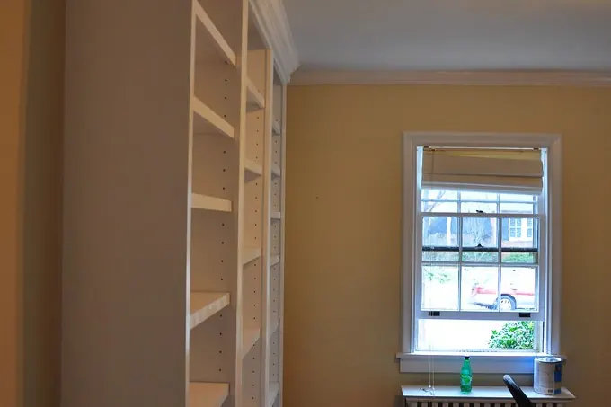A white painted built-in bookcase wall running floor to ceiling beside a window in a home of the kind found in San Clemente CA