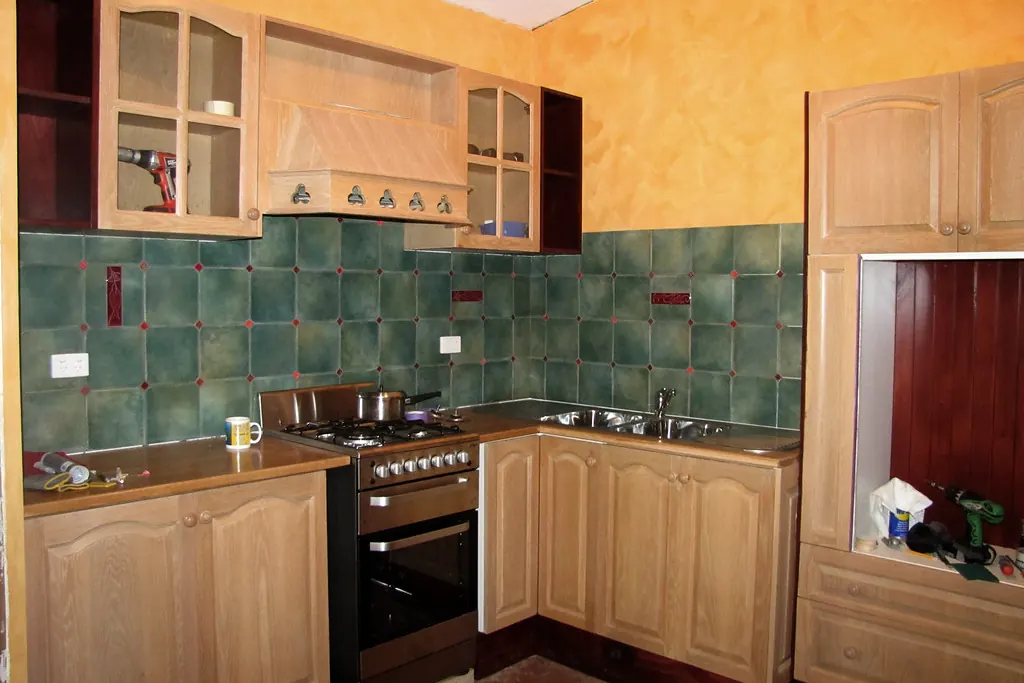An older kitchen with light oak arched panel doors, tiled splashback and a dated layout of the kind found in San Clemente CA tract housing