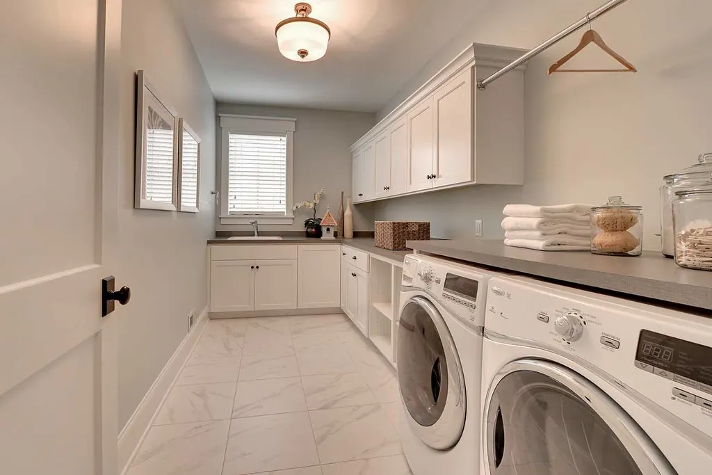 A white painted laundry room with wall cabinets, a folding counter, a hanging rail and front-loading machines in a San Clemente CA style home