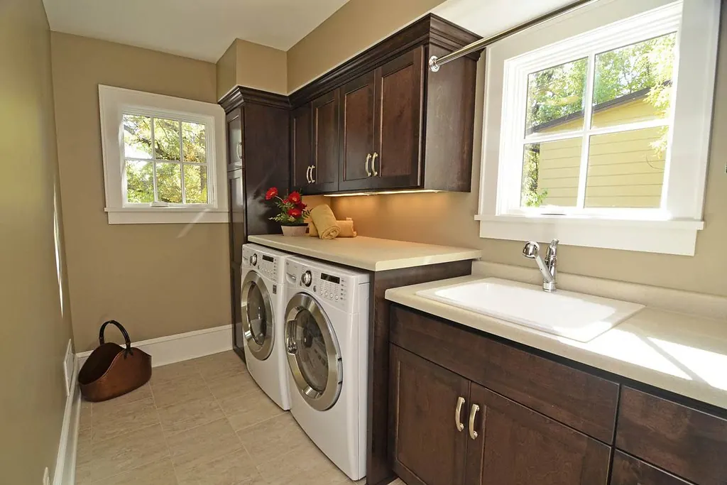 A laundry room with dark stained cabinets above front-loading machines, a sink and a folding counter in a Southern California home near San Clemente CA