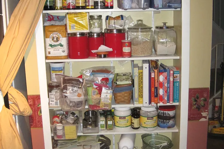 A fully loaded pantry closet with white shelves holding jars, tins and packets in a home of the kind found in San Clemente CA