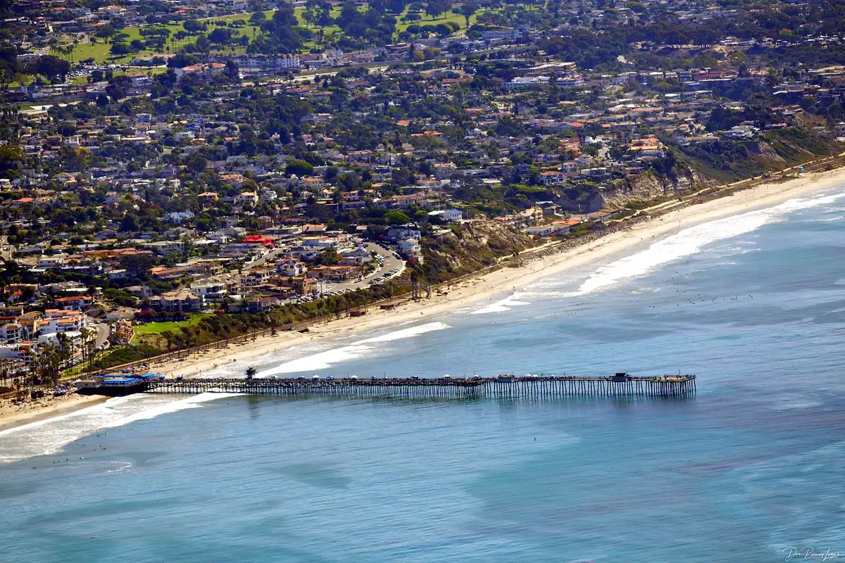 Aerial view of San Clemente CA showing the coastline, the pier and hillside housing across the city