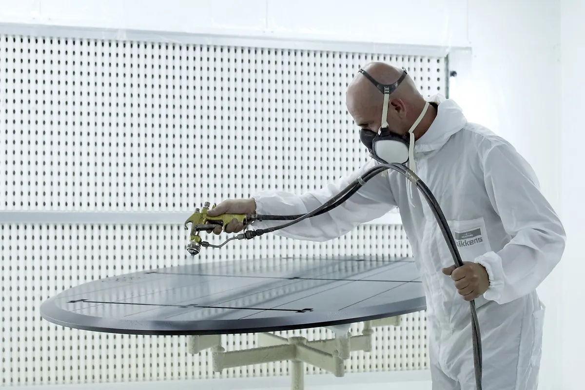 A finisher in a protective suit and respirator spraying a panel inside a professional spray booth, the way cabinets for San Clemente CA are finished