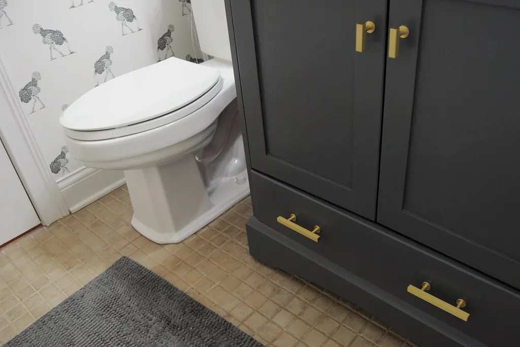A dark grey painted bathroom vanity with brass bar pulls and a tiled floor in a home of the kind found in San Clemente CA