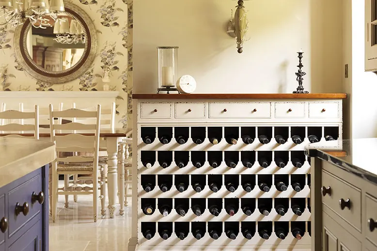 A built-in white cabinet run with bottle cubbies below a counter in a room with exposed dark ceiling beams, the condition found in older Capistrano Beach CA houses