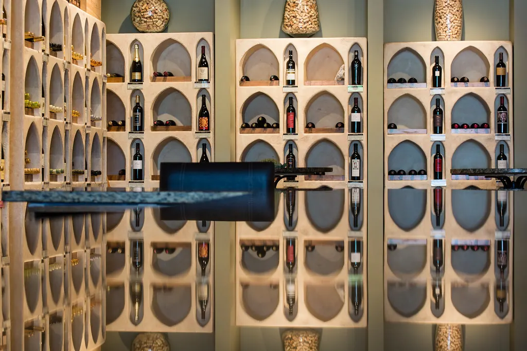 An illuminated wine wall with arched bottle niches and a glass counter in a home of the kind found in San Clemente CA